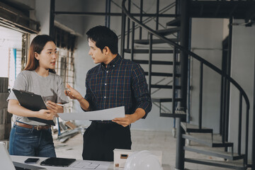 Construction manager and engineer dressed in orange work vests and hard helmets explore construction documentation on the building site near the steel frames