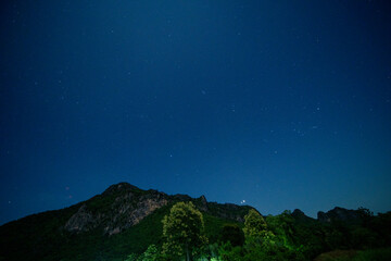 ฺBreathtaking view of star-filled night sky above lush green mountain range, serene beauty of nature under the vast cosmos.