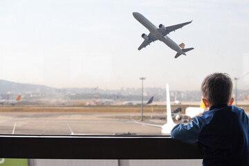 Kid watching planes taking off from airport window. Boy waiting for his flight. Aviation idea concept.	

