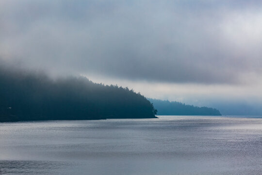 Clearing fog over forested point of land, East Sound, Orcas Island, WA USA