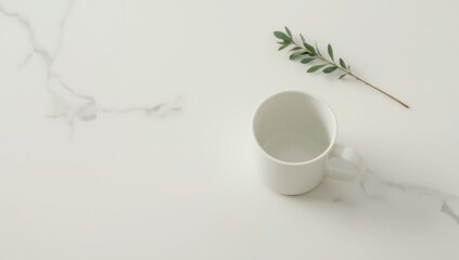 A pristine white mug sits on a marbled surface, accompanied by a delicate sprig of greenery, evoking a tranquil and minimalist aesthetic.