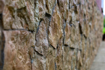 The surface of a stone wall with a rough, uneven texture. The stones have various shades of brown, gray, and yellow, and the joints between them are filled with cement. The photo showcases the natural