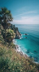 Fototapeta premium Scenic coastal view of azure water, rocky cliffs, lush vegetation & palms under a clear blue sky