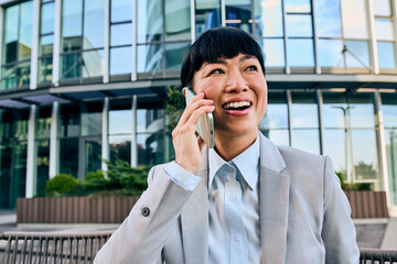 Asian Businesswoman Smiling While Talking On Phone Outside Modern Office Building