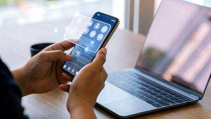 Person uses smartphone with futuristic interface beside laptop, showcasing modern technology and digital connectivity in a bright, contemporary workspace.