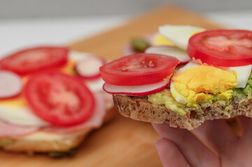 Eating sandwiches for breakfast. A half-bitten tomato, egg, and avocado sandwich held in the hand close-up