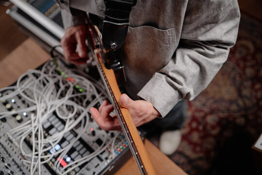 Caucasian man playing electric guitar next to audio mixer with multiple cables, focusing on hand positioning and instrument control in music production setting
