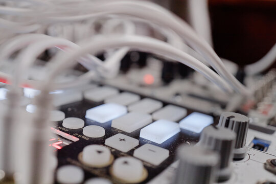 Electronic music production equipment featuring illuminated buttons, control knobs, and connected cables, close up showing details of audio interface and synthesizer controls