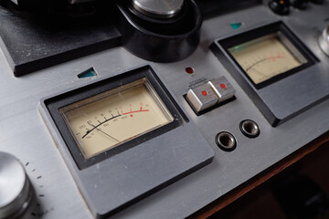 Closeup showing analog audio equipment with two vintage VU meters displaying signal levels, metallic control buttons and dials visible on professional recording device