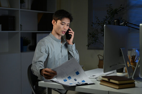 Asian businessman working late and checking documents while having phone call