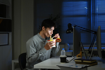 Asian young businessman eating noodles while working in office at night.