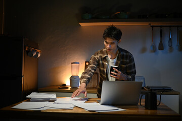 Focused man working late at night on laptop in kitchen with coffee