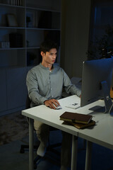 Staying late to get it done. Shot of a young businessman using a computer at his desk during a late night at work.