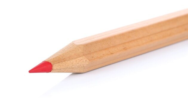 A light-brown colored pencil with a vibrant red tip lies angled on a plain white background.