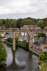 Fototapeta premium Monochrome image of a large stone viaduct with multiple arches, set against a dramatic cloudy sky and town buildings in the background