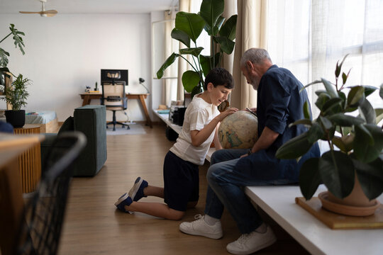 Grandfather teaching grandson geography with globe in living room