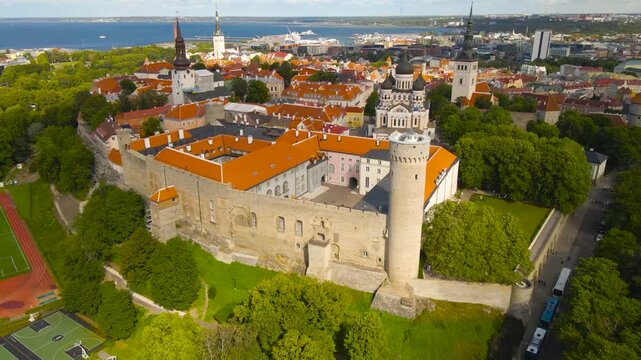 Aerial drone revealing shot of Tallinn old town historic medieval buildings and parliament building with Tall Hermann tower that has Estonian flag waving. Baltic sea and harbor visible in back, summer