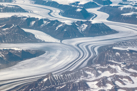 Aerial cockpit view of glacier flowing through mountains in Greenland