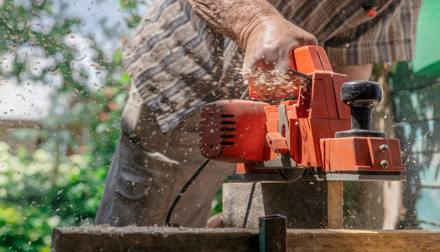 Close up of hand using electric planer on wood outdoors in backyard