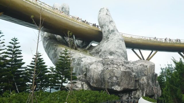 Golden bridge connecting ba na hills landscape, supported by massive stone hands, showcasing dramatic architectural marvel drawing visitors from worldwide