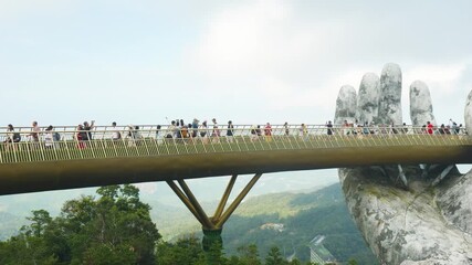 Tourists walking the golden bridge held by giant hands in ba na hills near da nang, vietnam, are enjoying the view of the surrounding landscape