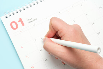 Female hand and calendar january 2026 on blue background top view.