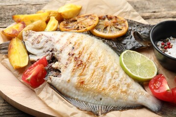 Tasty roasted flounder fish served with potatoes, tomatoes and lemon slices on wooden table, closeup. Homemade seafood dish
