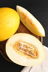 Cut and whole ripe melons on black wooden table, flat lay