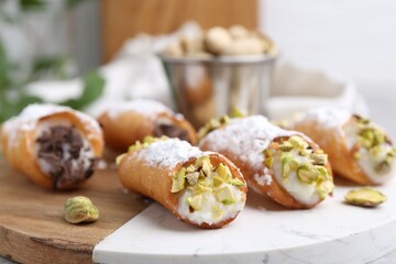 Delicious cannoli with ricotta cheese, pistachios, chocolate and powdered sugar on table against blurred background, closeup