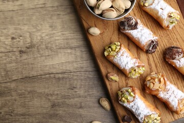 Delicious cannoli with ricotta cheese, peanuts, pistachios, chocolate and powdered sugar on wooden table, flat lay. Space for text