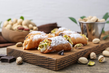 Delicious cannoli with ricotta cheese, peanuts, pistachios, chocolate and powdered sugar on wooden table against light grey background, closeup