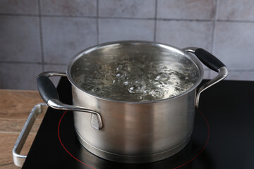 Metal pot with boiling water on stove in kitchen, closeup