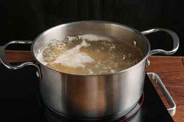 Fresh tagliatelle pasta boiling in pot with water on electric stove, closeup