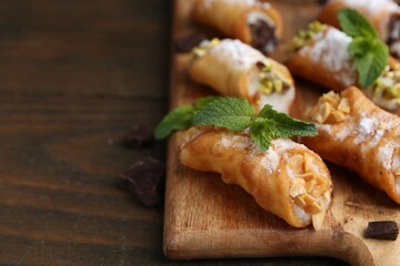 Delicious cannoli with cheese, nuts, chocolate, mint and powdered sugar on wooden table, closeup. Space for text