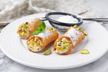 Delicious cannoli with cheese, pistachios, powdered sugar and mint on white marble table, closeup
