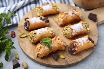 Delicious cannoli with cheese, nuts, powdered sugar, chocolate and mint on grey table, closeup