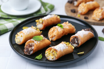Delicious cannoli with cheese, nuts, powdered sugar, chocolate and mint on white table, closeup