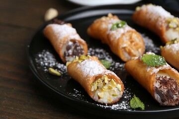Delicious cannoli with cheese, nuts, powdered sugar, chocolate and mint on wooden table, closeup