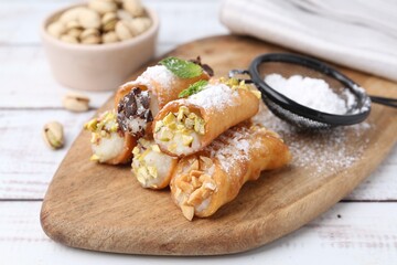 Delicious cannoli with cheese, nuts, powdered sugar, chocolate and mint on white wooden table, closeup