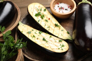 Halves of fresh eggplant, whole ones, spices and parsley on wooden table, closeup