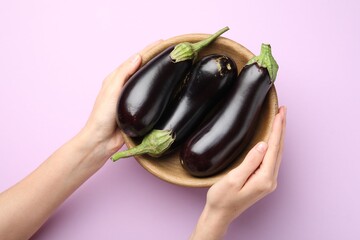 Woman with bowl of fresh eggplants on violet background, top view