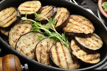 Grilled slices of eggplant with microgreens served on wooden table, closeup