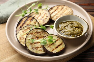 Grilled slices of eggplant with sauce and microgreens on wooden table, closeup