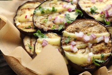 Grilled slices of eggplant with sauce, parsley and onion served on wooden table, closeup