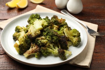 Tasty fried broccoli, fork and lemon on wooden table, closeup