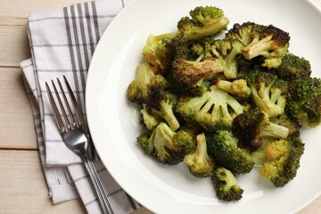 Tasty fried broccoli and fork on light wooden table, top view