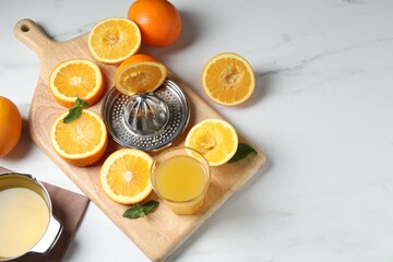 Squeezer with oranges, mint and fresh juice on white table, flat lay. Space for text
