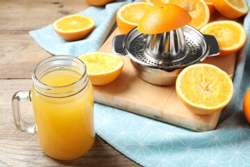 Freshly squeezed orange juice, fruits, juicer and towel on wooden table, closeup