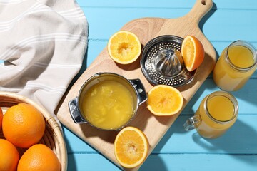 Freshly squeezed orange juice, fruits, juicer and towel on blue wooden table, flat lay