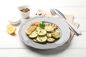 Delicious fried courgette slices with lemon and parsley served on white wooden table, closeup